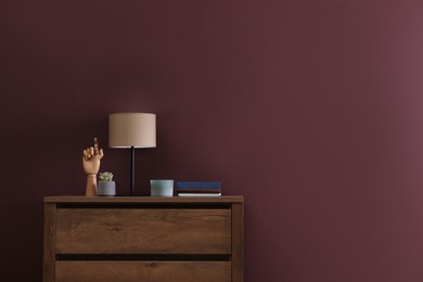 Photo of Books, decor and lamp on chest of drawers near brown wall indoors, space for text. Interior design