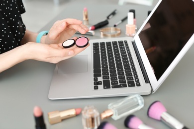 Photo of Young woman with makeup products using laptop at table. Beauty blogger