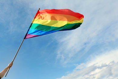 Photo of Gay man holding rainbow LGBT flag against blue sky. Space for text