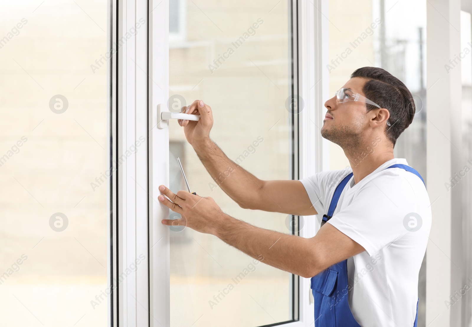 Photo of Construction worker repairing plastic window with screwdriver indoors