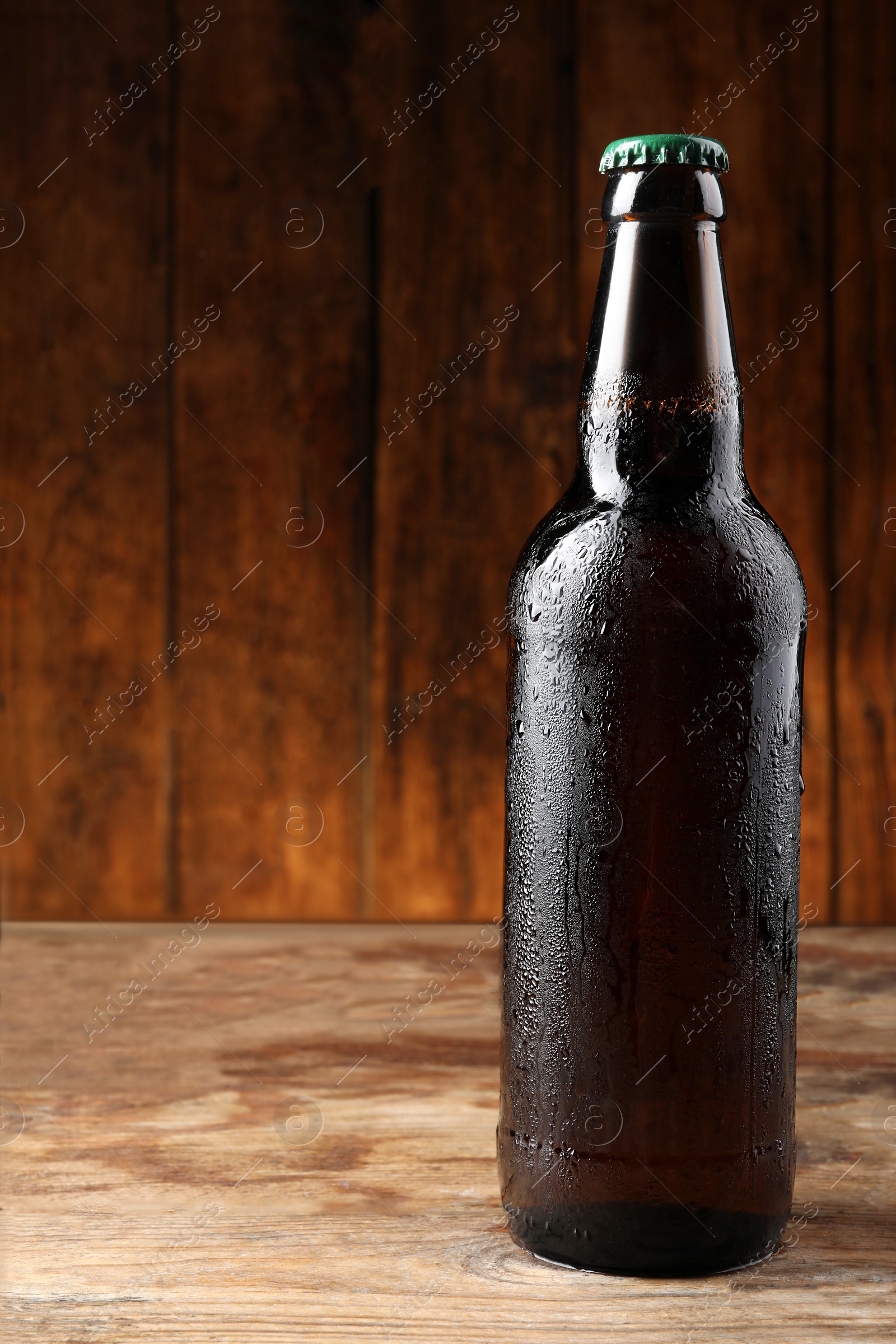 Photo of Glass bottle of beer on wooden table, space for text