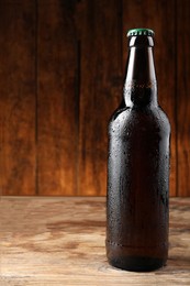 Glass bottle of beer on wooden table, space for text
