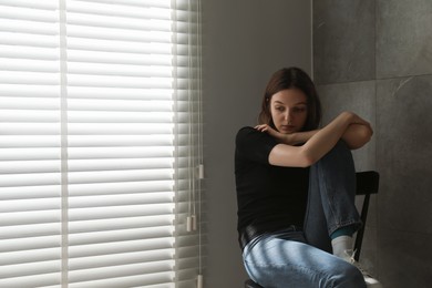 Sad young woman sitting on chair indoors, space for text