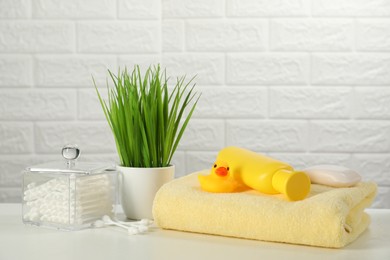 Photo of Baby bath accessories. Towel, cosmetic products, cotton swabs and toy duck on white table against brick wall