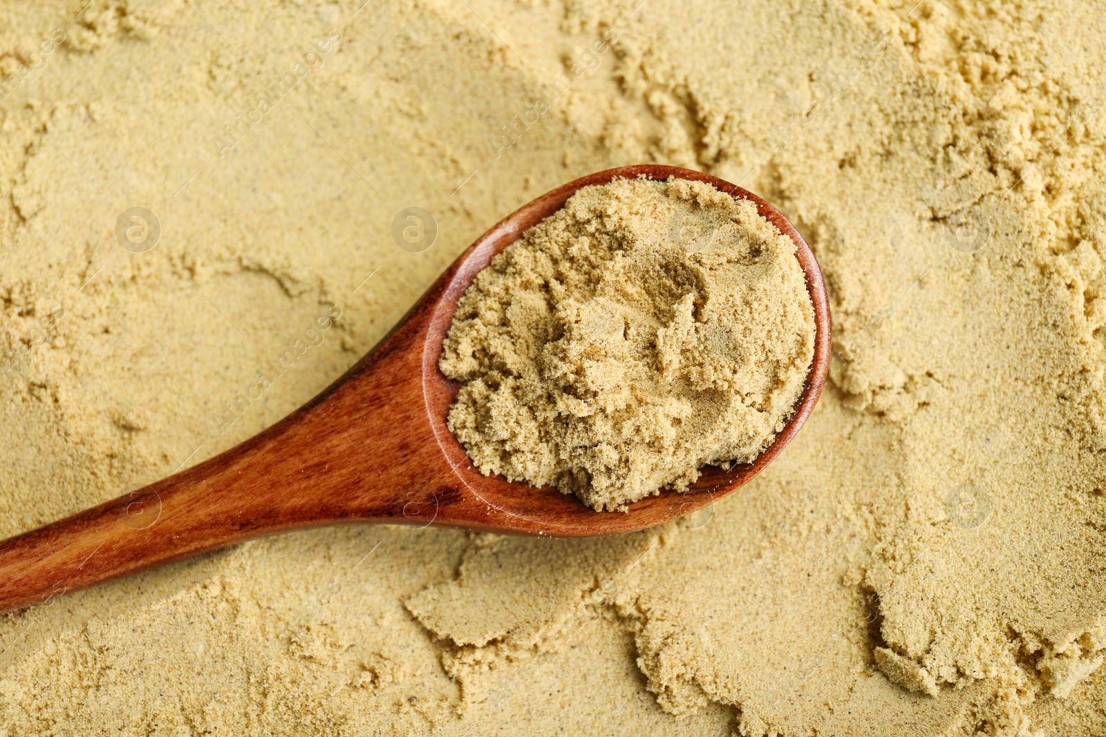 Photo of Heap of aromatic mustard powder and wooden spoon, top view