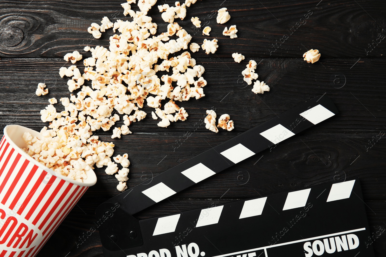 Photo of Tasty popcorn and clapperboard on wooden background, top view. Cinema snack