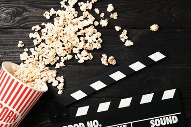 Tasty popcorn and clapperboard on wooden background, top view. Cinema snack