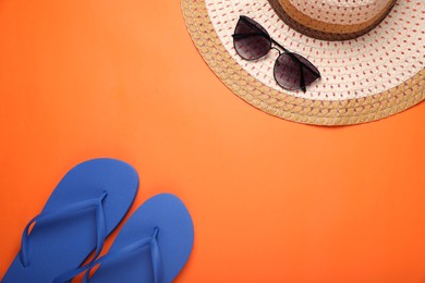 Photo of Stylish blue flip flops, sunglasses and hat on orange background, flat lay. Space for text