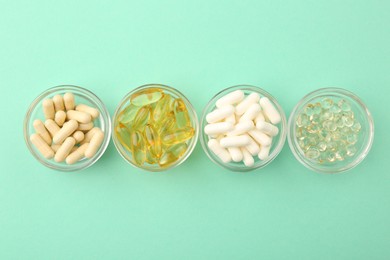 Different vitamin capsules in glass bowls on turquoise background, flat lay
