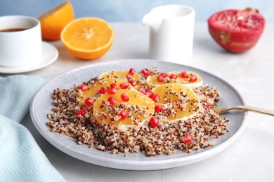 Photo of Plate of quinoa porridge with orange and pomegranate seeds served for breakfast on table