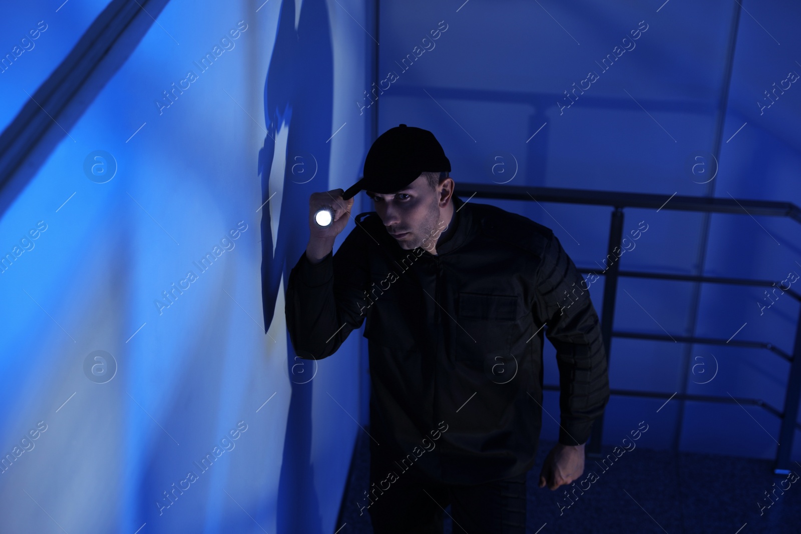 Photo of Male security guard with flashlight on stairs in darkness