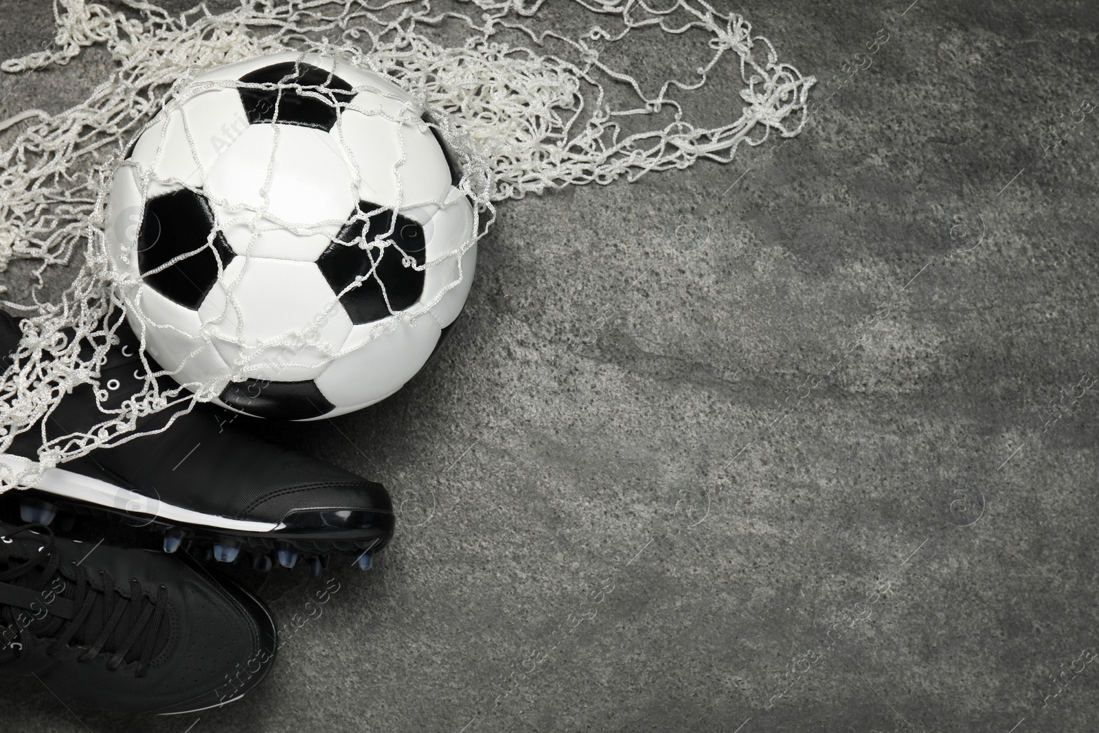 Photo of Sports equipment. Soccer ball, net and sneakers on grey textured table, flat lay. Space for text