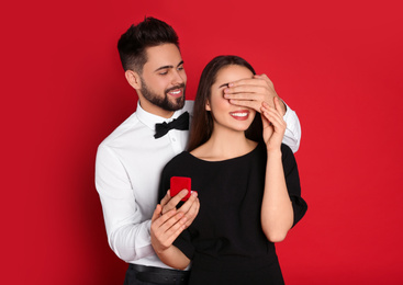 Man with engagement ring making marriage proposal to girlfriend on red background