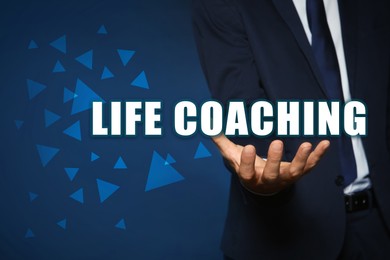 Image of Personal development concept. Businessman holding virtual phrase Life Coaching on blue background, closeup
