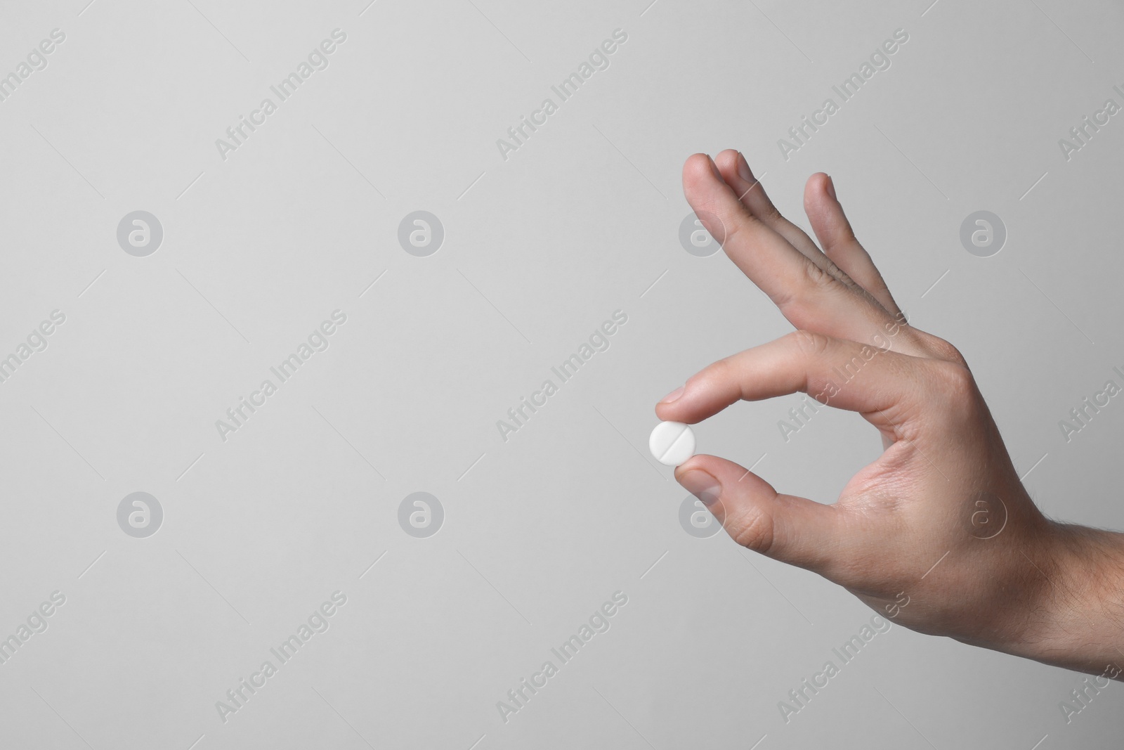 Photo of Man holding pill on light grey background, closeup. Space for text