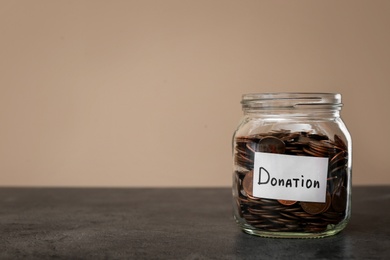 Photo of Donation jar with coins on table  against color background. Space for text