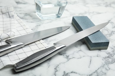 Photo of Sharpening stone and knives on white marble table, closeup