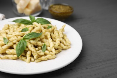 Plate of delicious trofie pasta with pesto sauce and basil leaves on grey wooden table, closeup. Space for text