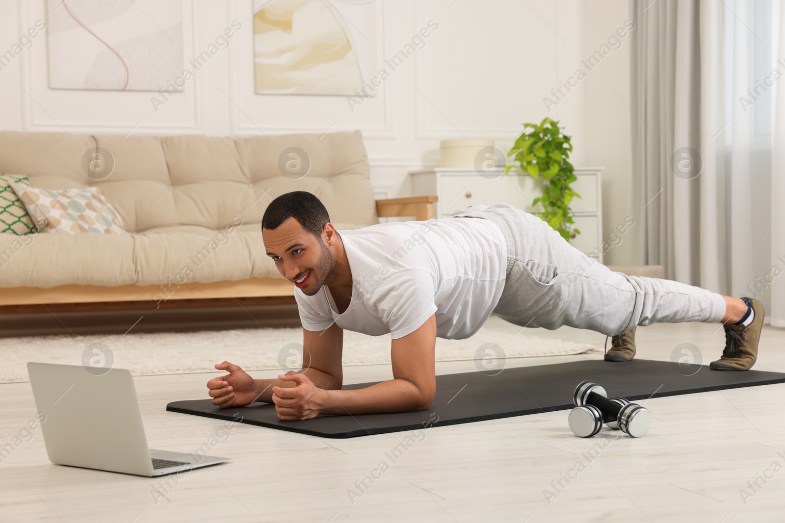 Photo of Man doing morning exercise on fitness mat near laptop at home
