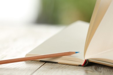Closeup view of open notebook with pencil on white wooden table against blurred background
