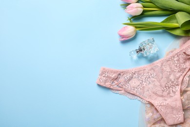 Photo of Elegant beige women's underwear, perfume and beautiful tulips on light blue background, flat lay. Space for text