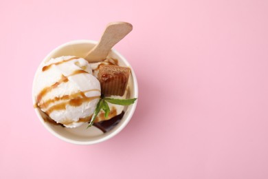 Photo of Tasty ice cream with caramel sauce, mint and candy in paper cup on pink background, top view. Space for text