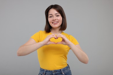 Photo of Happy woman showing heart gesture with hands on grey background