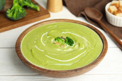 Photo of Delicious broccoli cream soup served on white wooden table, closeup