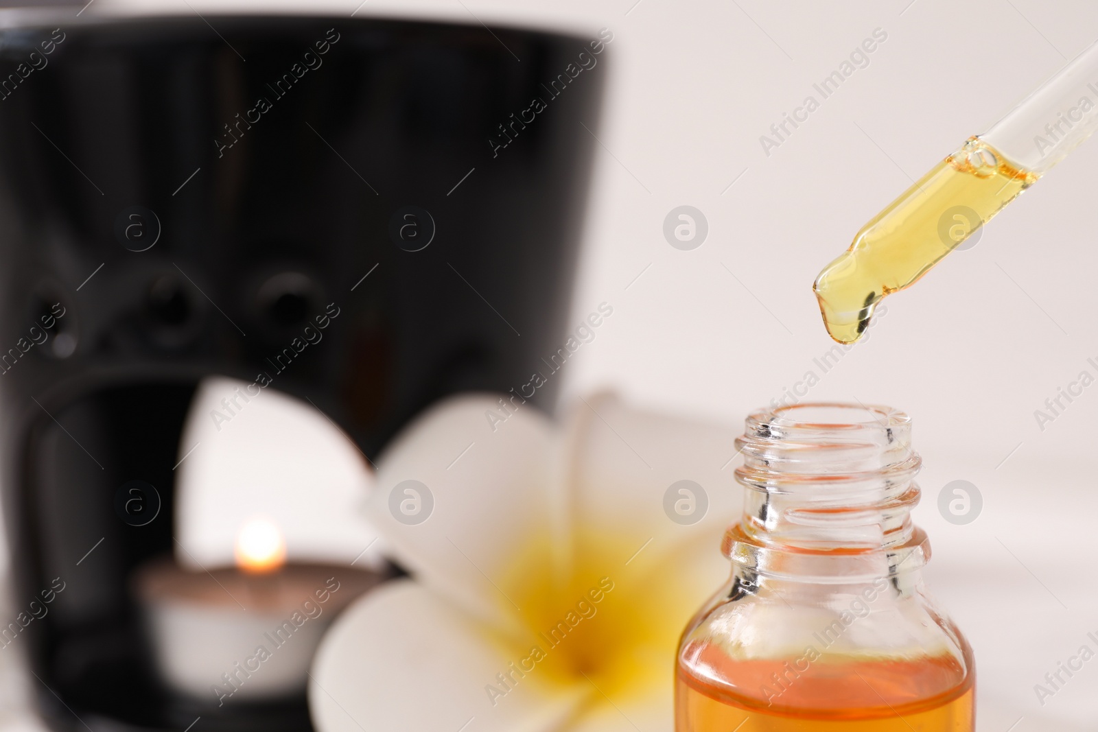 Photo of Aroma lamp against white background, focus on dripping of essential oil into bottle, closeup. Space for text