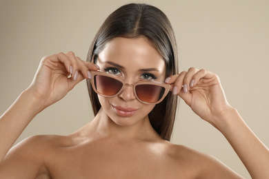 Photo of Beautiful young woman wearing sunglasses on beige background
