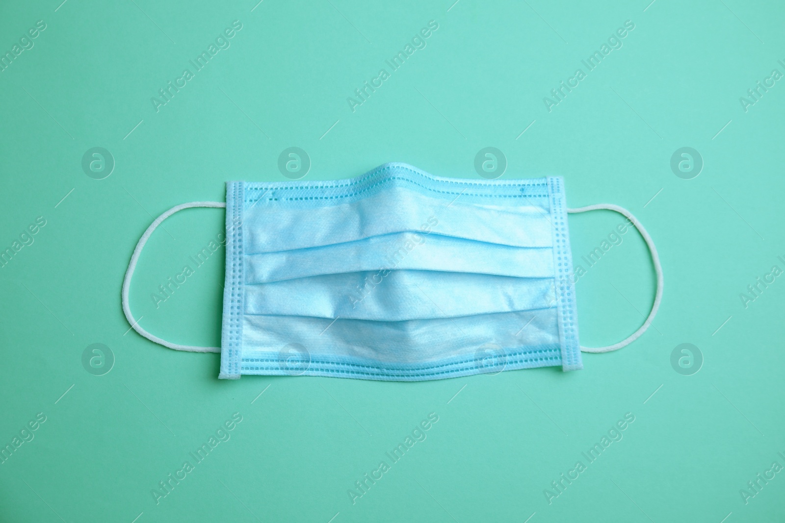 Photo of Medical face mask on turquoise background, top view