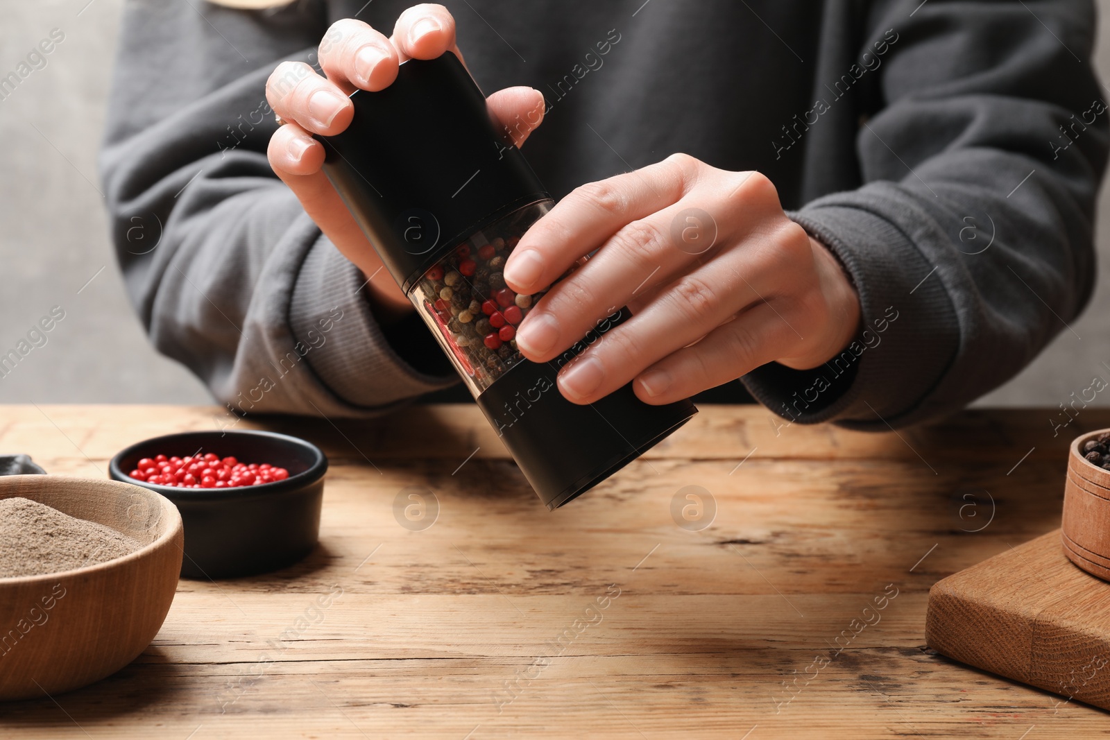 Photo of Woman grinding pepper with shaker at wooden table, closeup