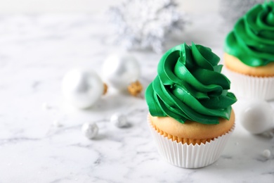 Photo of Delicious cupcakes with green cream and Christmas decor on white marble table. Space for text