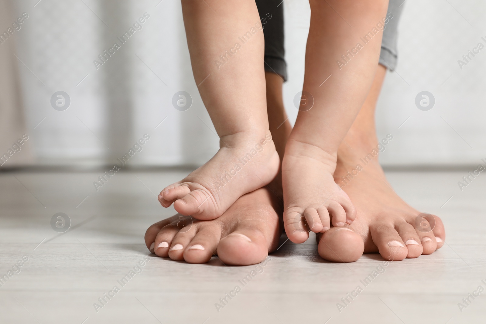 Photo of Woman and her little child standing on floor indoors, closeup. Space for text