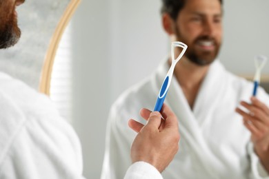 Photo of Happy man with tongue cleaner near mirror in bathroom, selective focus