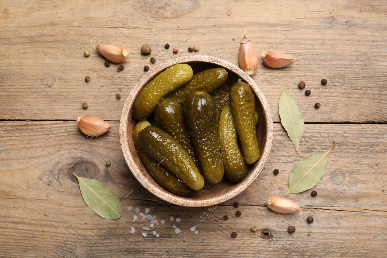 Photo of Tasty pickled cucumbers in bowl and spices on wooden table, flat lay