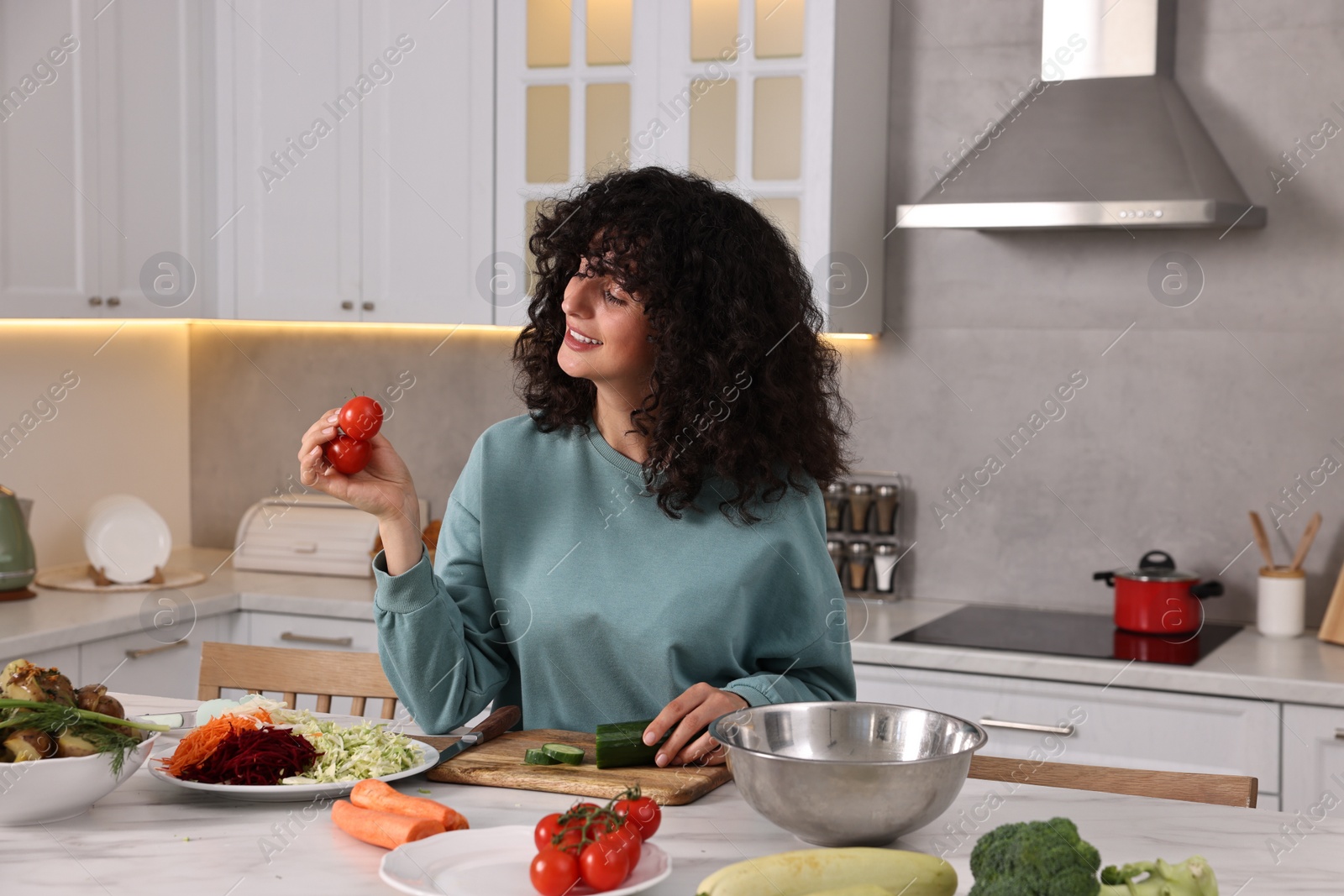 Photo of Woman cooking healthy vegetarian meal at white marble table in kitchen