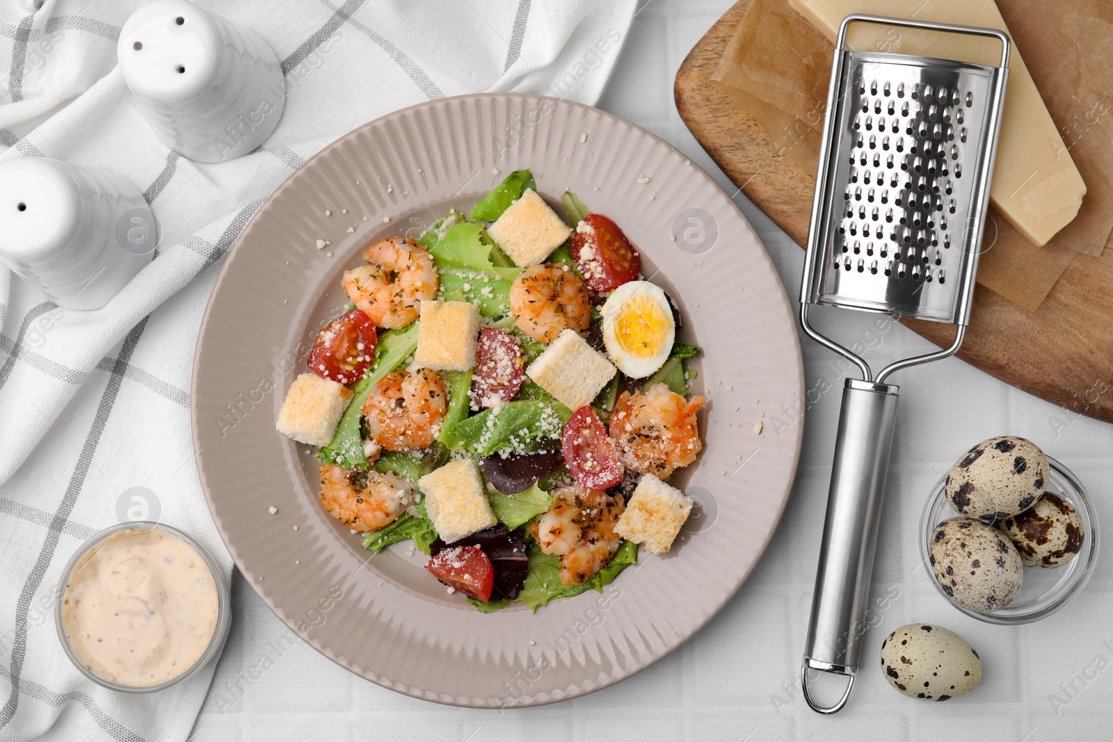 Photo of Delicious Caesar salad with shrimps and ingredients on white tiled table, flat lay