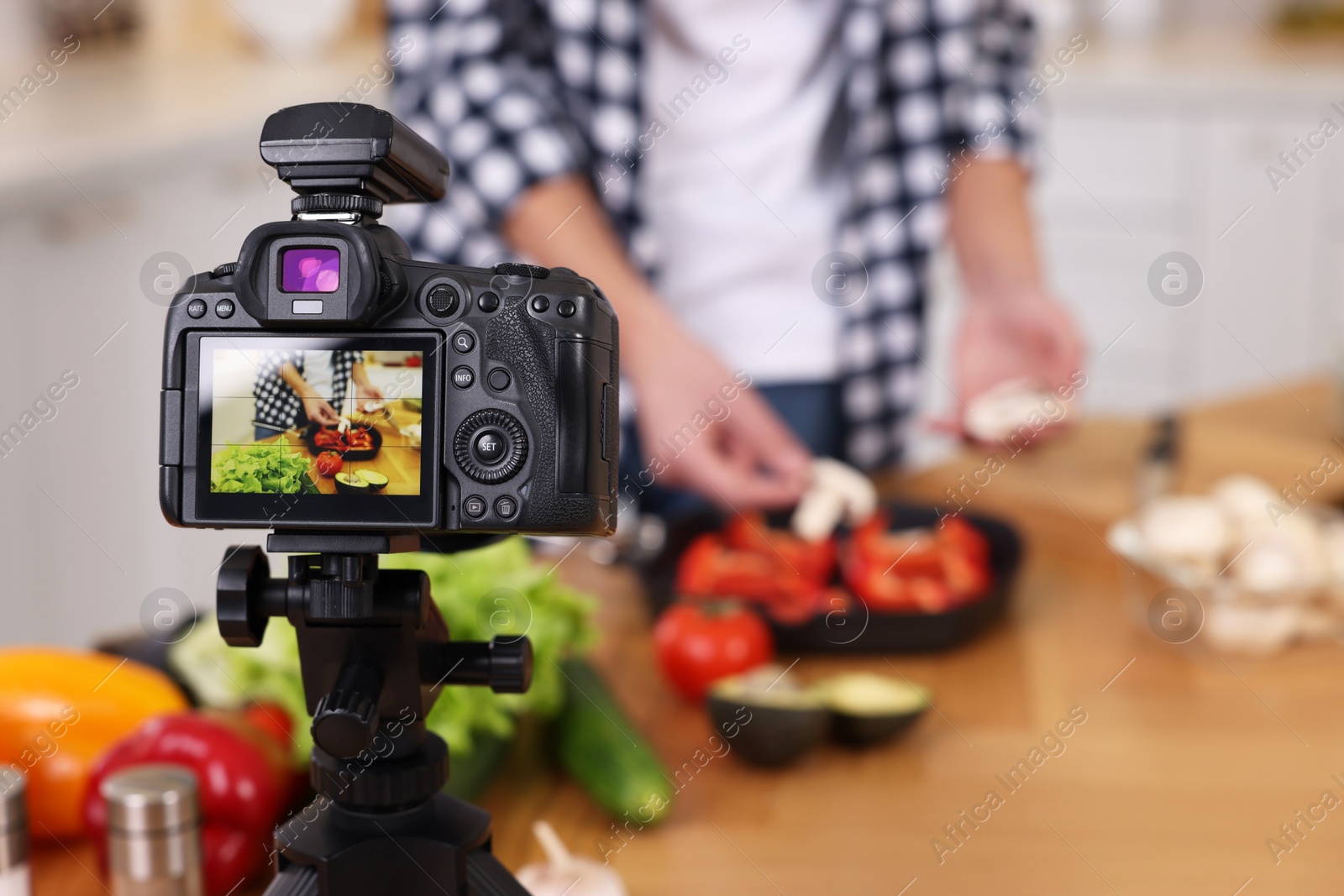 Photo of Food blogger cooking while recording video in kitchen, focus on camera