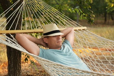 Photo of Man with hat resting in comfortable hammock at green garden