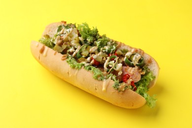 Photo of Delicious hot dog with chili peppers, lettuce, pickles and sauces on yellow background, closeup
