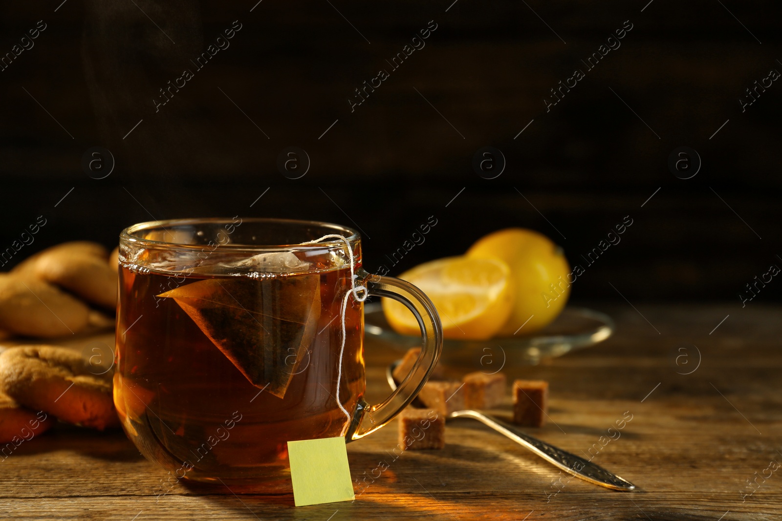 Photo of Tea bag in glass cup of hot water on wooden table against dark background, space for text