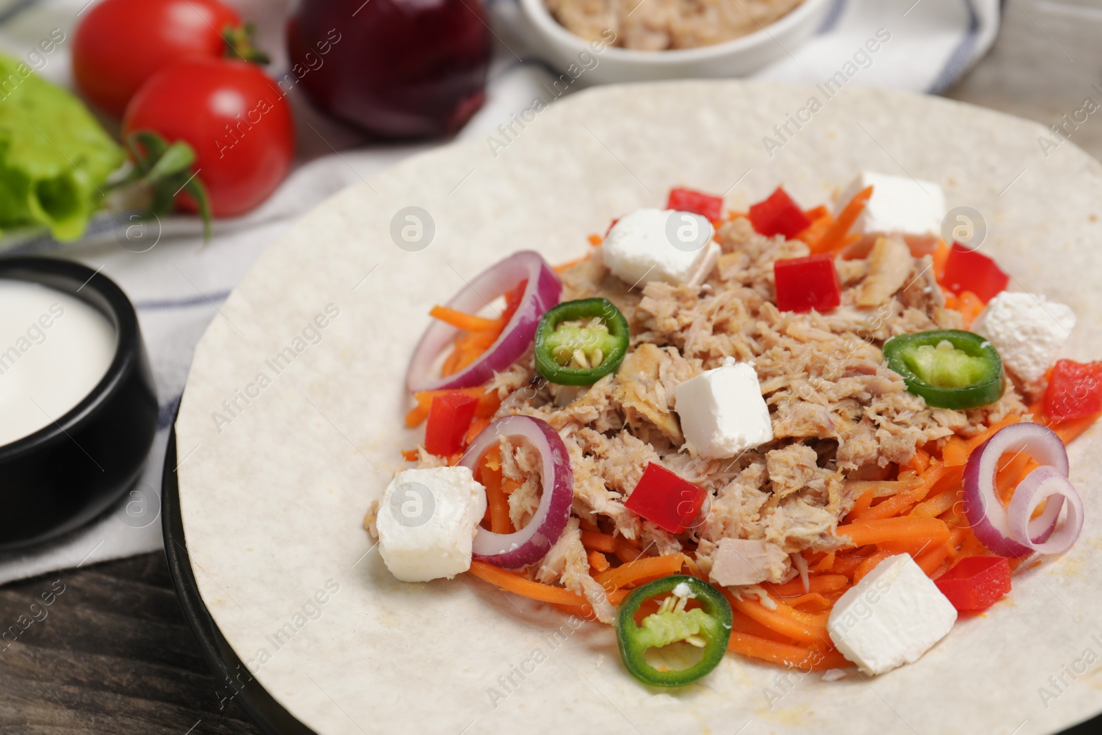 Photo of Delicious tortilla with tuna, vegetables and cheese on wooden table, closeup. Cooking shawarma