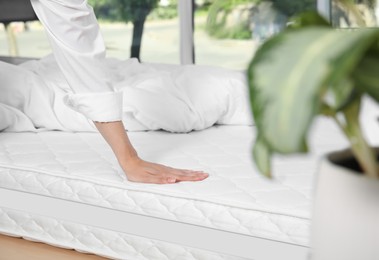 Woman touching soft white mattress on bed indoors, closeup