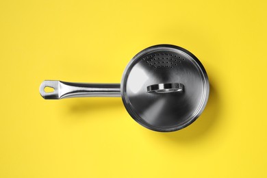 Steel saucepan with lid on yellow background, top view