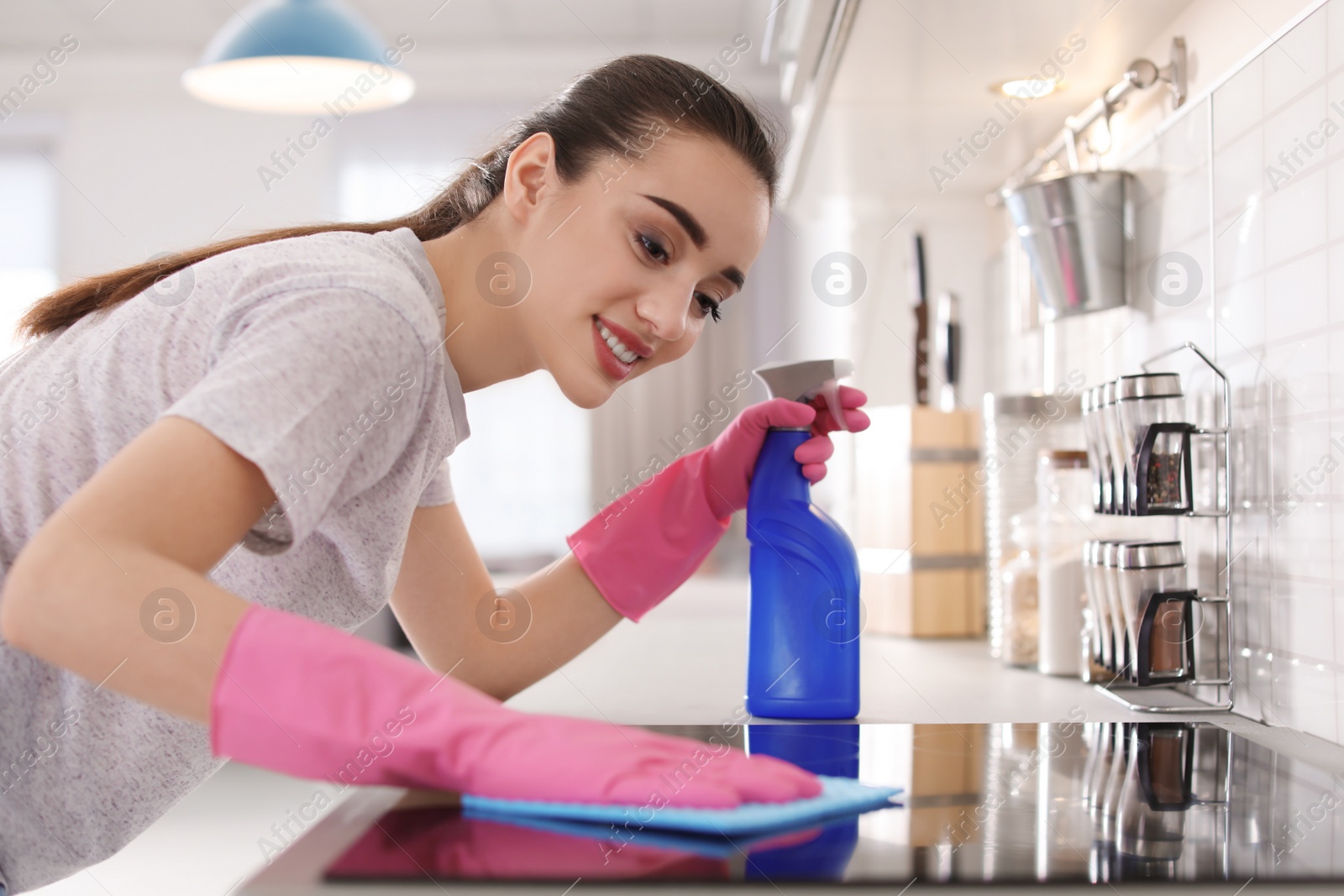 Photo of Young woman cleaning stove with rag in kitchen