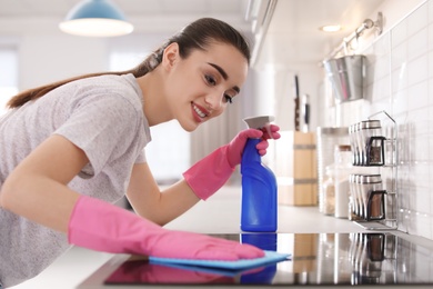 Young woman cleaning stove with rag in kitchen