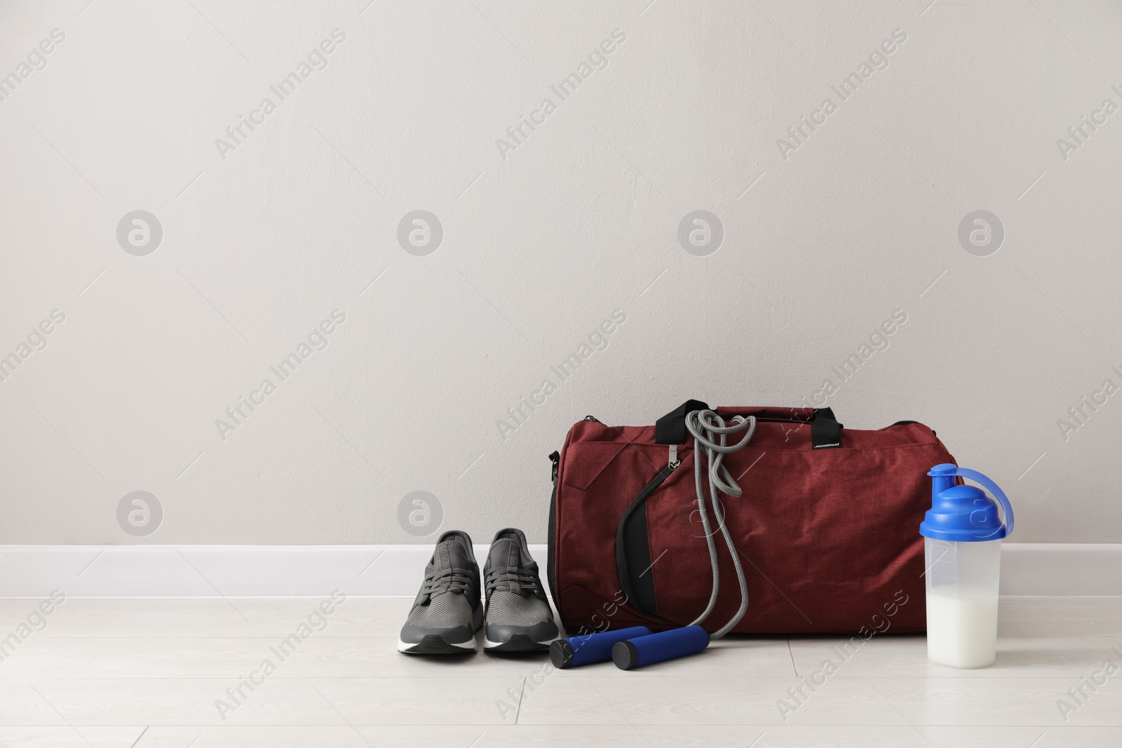 Photo of Red bag and sports accessories on floor near light wall, space for text