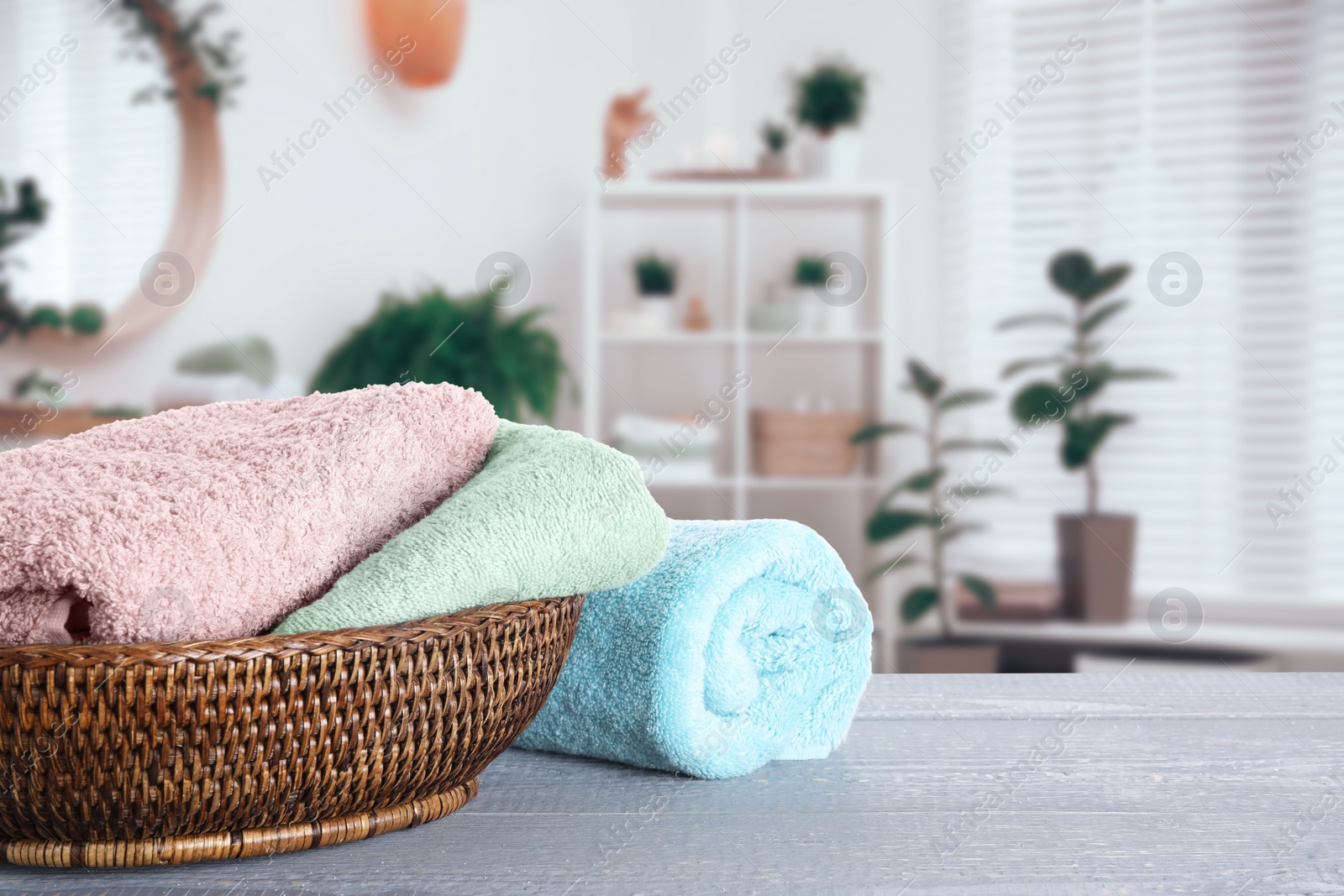 Image of Wicker basket with clean soft towels on grey wooden table in bathroom. Space for text