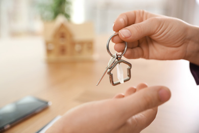 Photo of Real estate agent giving key with trinket to client in office, closeup